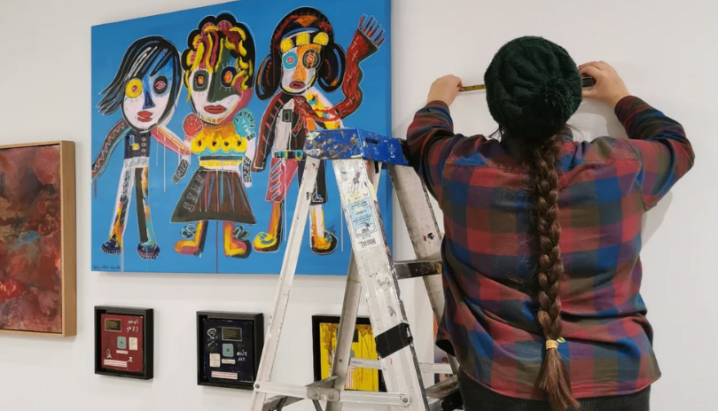 A person on a ladder measures a wall in an art gallery.
