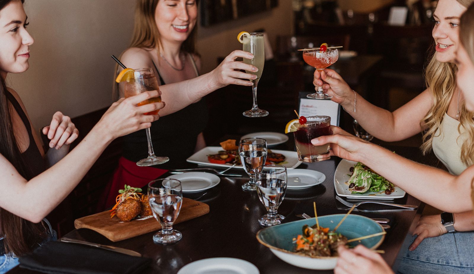 four people at a dinner table holding glasses toasting each other