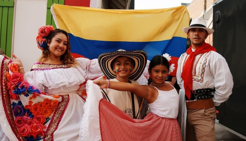 A family in traditional outfits stands in front of a Colombian flag.
