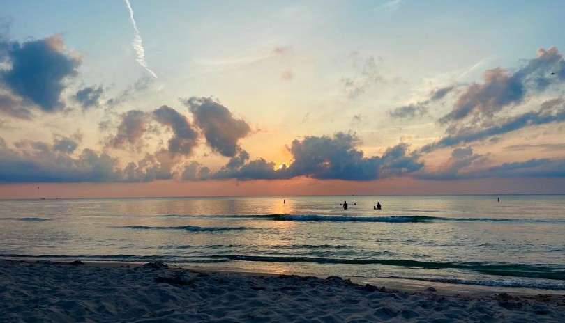 The shore of Grand Bend's beach with people swimming in the water while the sun is setting