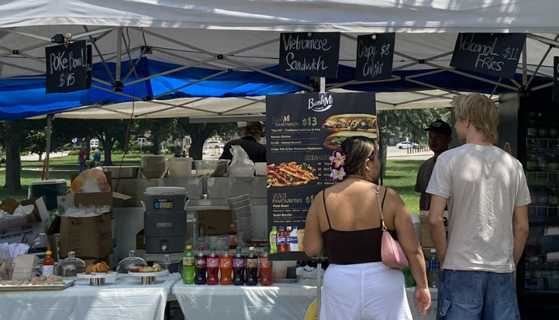 A couple stands at a street food vendor's booth at an outdoor food festival.