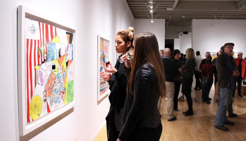 A crowd of people look at art during a gallery opening.