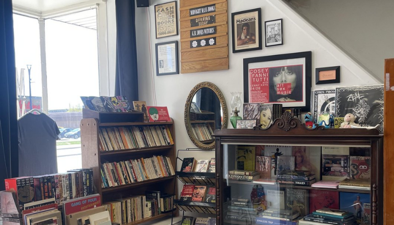 A bookshelf lit by natural light from a large window in Midnight Mass Books in London, Ontario.