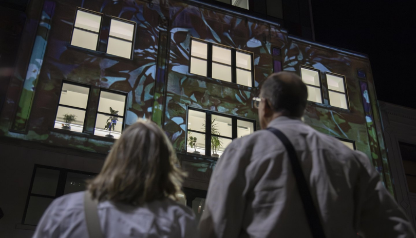 Two people look up at a building covered in light projections during Nuit Blanche in London, Ontario.