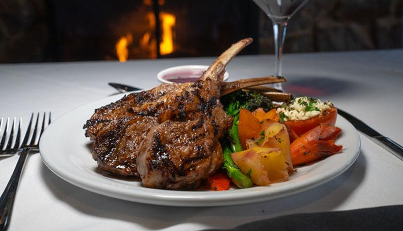 three lamb chops on a white plate with brightly coloured vegetables