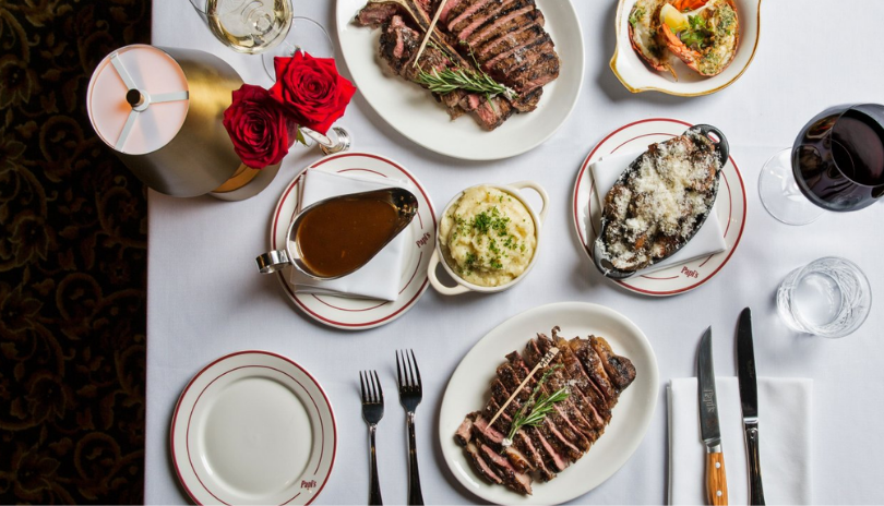 An overhead view of a fine dining table set with steaks and wine.