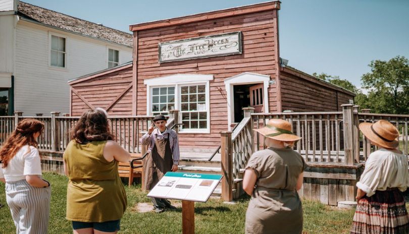 a small group of people listening to a tour guide in front of a historic building at Fanshawe Pioneer Village located in London, Ontario 