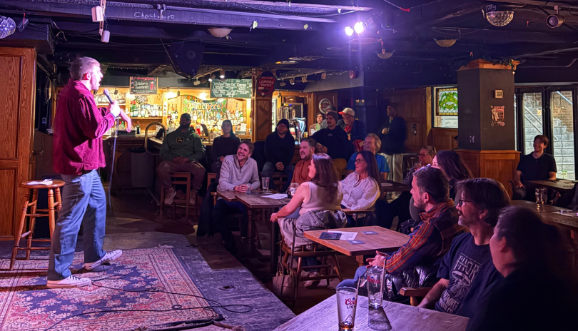 A crowd of people sit and watch a stand-up comic onstage at Poacher's Arms bar in London, Ontario.