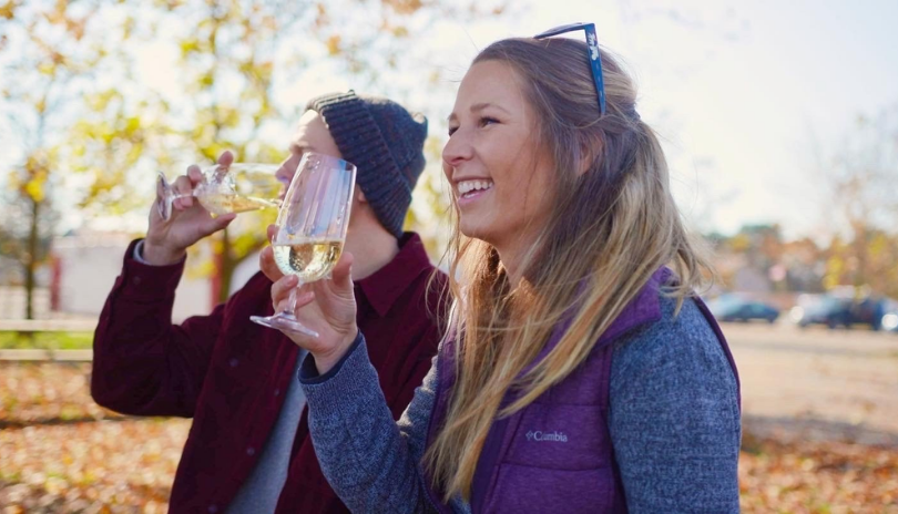 Two people sip wine outside on a fall day.