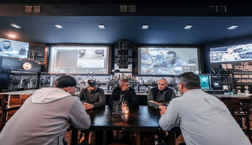 A group of friends seated inside of The Squire Pub & Grill's main dining area in front of the bar with sports playing on various TV screens located in London, Ontario