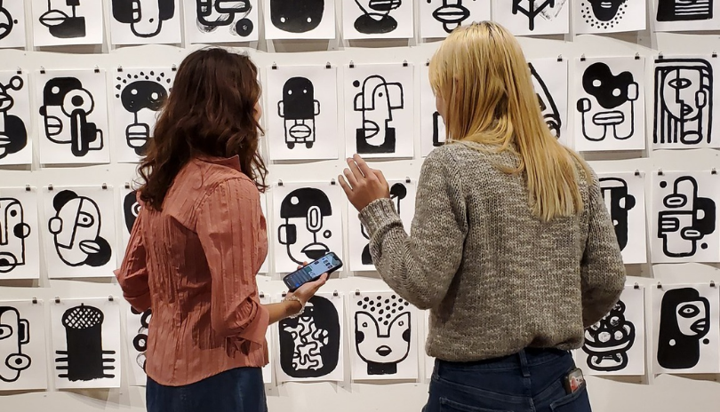 Two women stand in front of a series of small cartoon paintings at TAP Centre for Creativity.