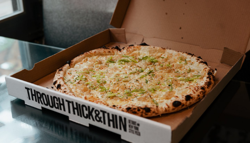 An open box of pizza sits on a glass table.