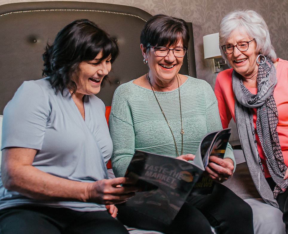 three people sitting on a bed reading a magazine