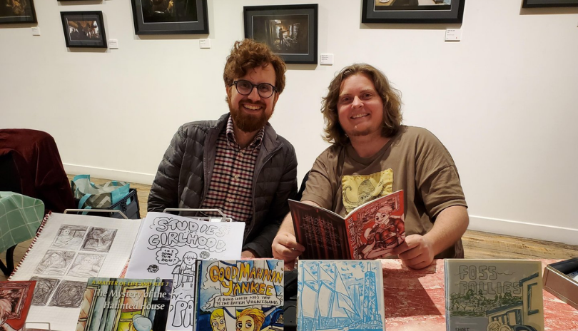 Two artists sit behind a vendor table in a gallery at TAP Centre for Creativity in London, Ontario.