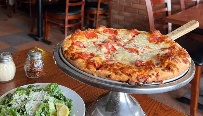 A pizza on a stand and a salad in Tony's Famous Italian in London, Ontario.