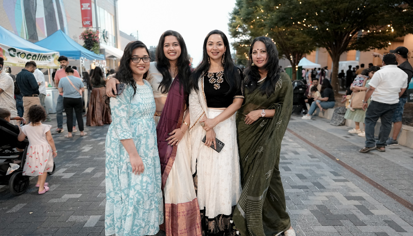 Four women in cultural clothing stand on a street during a summer festival.