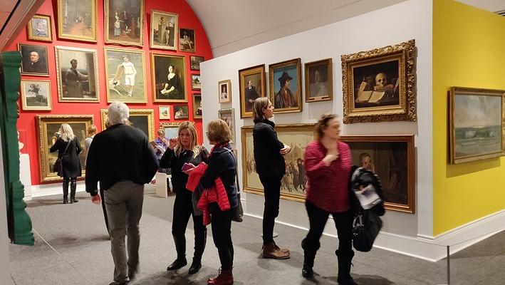 A group of people observing various paintings on display at Museum London located in London, Ontario