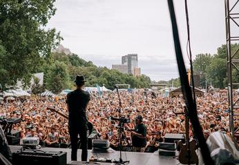 A singer on stage looking out to a large crowd outdoors in Harris Park at the Rock the Park Festival