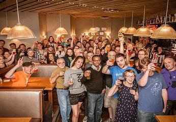 A large crowd of people holding glasses of beer and smiling at Milos' Craft Beer Emporium located in London, Ontario