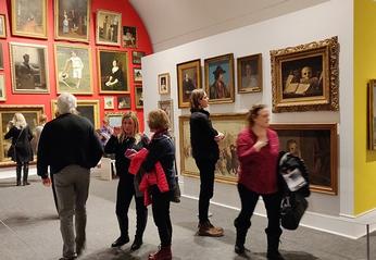 A group of people observing various paintings on display at Museum London located in London, Ontario