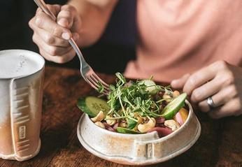 A person seated at a wood table eating a fresh salad from The Root Cellar located in London, Ontario