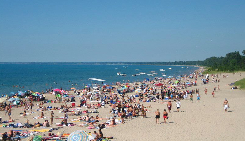 Large groups of people gathered at a beach in Grand Bend on a hot summer day