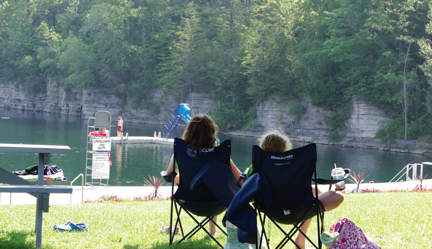 A mother and her daughter siting on lawn chairs looking at a dock and body of water on a hot summer day in St, Marys, Ontario