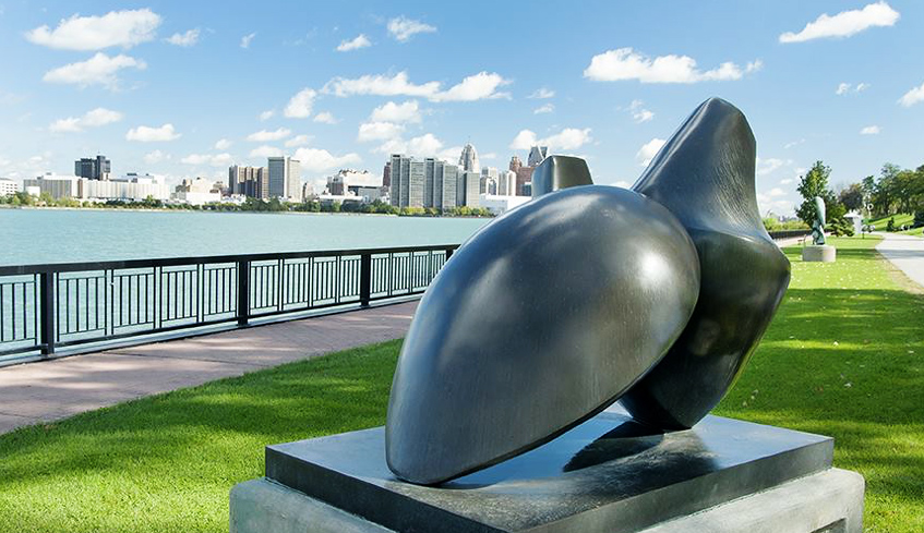 A metal sculpture beside a paved walking path overlooking the Detroit River in Windsor, Ontario