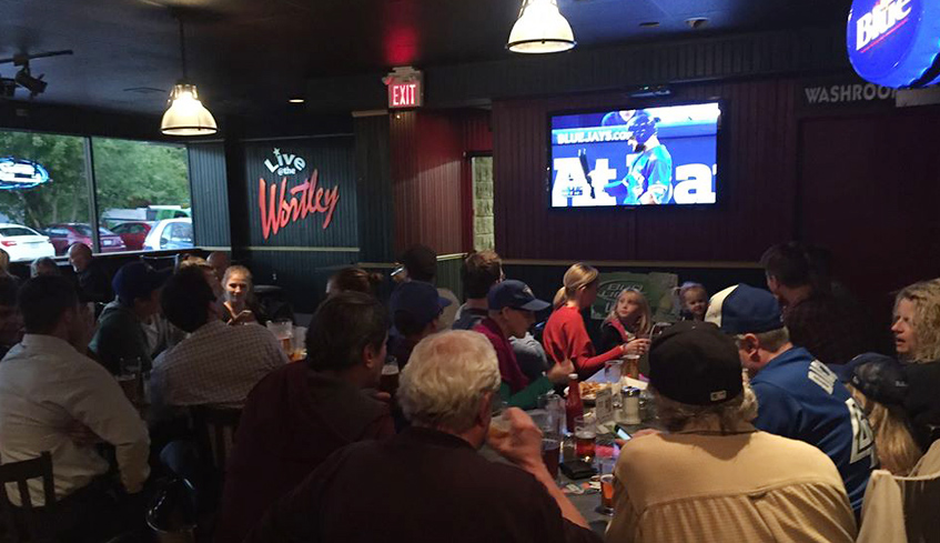 Groups of people seated inside of The Wortley Roadhouse's main dining area with sports playing on a TV screen located in London, Ontario